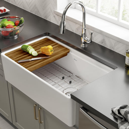 White farmhouse sink fitted with a wood cutting board and protective grid